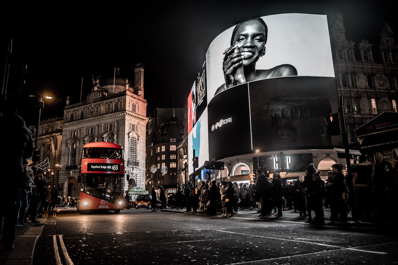 Home Vibrant city life at night in Piccadilly Circus, London with double-decker bus and illuminated billboards.